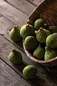 Closeup of round wicker bowl full of green figs lying on wooden table