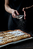 Crop shot of woman covering freshly baked frangipane apple pie with powdered sugar on wooden table