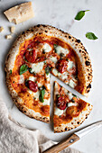 Draufsicht auf eine leckere Pizza mit Basilikum und Tomatensauce auf einem Holztisch neben einer Serviette in der Küche