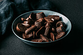 Assorted dark chocolate truffles and pralines in various shapes in bowl placed on black table