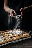 Crop shot of woman covering freshly baked frangipane apple pie with powdered sugar on wooden table