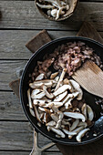 Top view of frying pot with sliced shiitake mushrooms and wood spatula on board