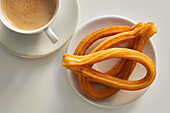 Appetizing churros on plate and cup of fresh morning coffee served on table for breakfast in kitchen