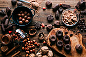 Top view of various handmade chocolates with nuts arranged on wooden table with peanut butter and cinnamon sticks