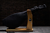 Delicious dry cured Spanish pork leg wrapped in black bag on wooden holder on gray surface