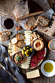 From above appetizing snack plate with several sorts of cheese,olives, pork loin and freshly baked bread on wooden table