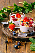 Von oben köstlicher hausgemachter Joghurt mit Erdbeeren, Beeren und Müsli auf Holztisch Hintergrund