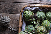 Closeup from above view of green artichokes laid in wicker basket with bunch of little purple flowers