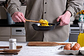 Unrecognizable crop male chef with delicious cooked Spanish omelette in frying pan standing at table in kitchen at home