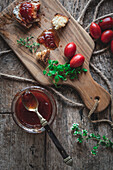 Top view of chopping board with bread and herbs placed near jar of tomato jam on lumber table in rustic kitchen