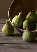 Closeup of round wicker bowl full of green figs lying on wooden table