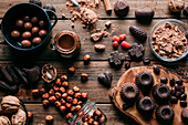 Top view of various handmade chocolates with nuts arranged on wooden table with peanut butter and cinnamon sticks