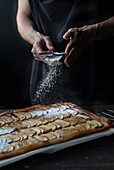 Crop shot of woman covering freshly baked frangipane apple pie with powdered sugar on wooden table