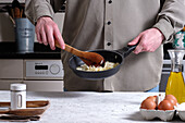Unrecognizable crop male chef frying onion in pan while cooking traditional Spanish omelet in kitchen