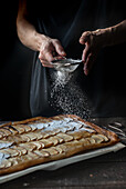 Crop shot of woman covering freshly baked frangipane apple pie with powdered sugar on wooden table
