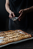 Crop shot of woman covering freshly baked frangipane apple pie with powdered sugar on wooden table