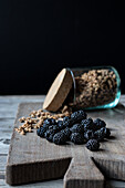 Blick von oben auf ein Glas mit Walnuss-Müsli und einen Haufen Blaubeeren auf einem Holzbrett vor schwarzem Hintergrund