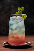 Glas Regenbogenparadies bunter Cocktail garniert mit Minzblatt auf Metalltablett