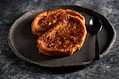 High angle of delicious homemade torrija with crunchy crust placed on black plate with spoon on marble table