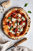 Top view of delicious pizza with basil and tomato sauce placed on wooden table near napkin in kitchen