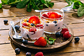 Köstlicher hausgemachter Joghurt mit Erdbeeren, Beeren und Müsli auf einem Holztisch im Hintergrund
