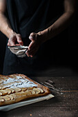 Crop shot of woman covering freshly baked frangipane apple pie with powdered sugar on wooden table