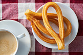 Appetitliche Churros auf einem Teller und eine Tasse frischen Morgenkaffee auf einer Serviette auf dem Frühstückstisch in der Küche