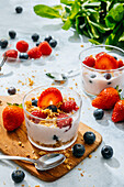 Von oben köstlicher hausgemachter Joghurt mit Erdbeeren, Beeren und Müsli auf weißem Hintergrund