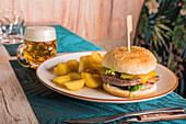 Delicious burger and potatoes on plate served on table with glass of fresh beer in cafe