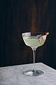 Glass goblet of martini cocktail garnished with red pepper served on table against black background