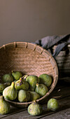 Closeup of round wicker bowl full of green figs lying on wooden table