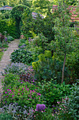 Blühender Garten mit gepflastertem Weg und üppiger Vegetation im Sommer