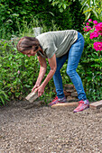 Woman building bed edging from old bricks and clinker bricks for bed with pre-grown young plants for planting