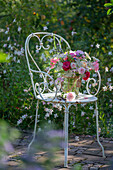 Bouquet of roses, wild carrot, flowering oregano, perennial vetch, autumn anemone and bearded flower on iron chair