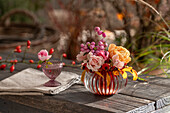 Bouquet of roses (Rosa) and snowberry (Symphoricarpos) 'Amethyst' in vase on garden bench