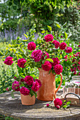 Bouquet of bourbon rose 'Vivid' (Rosa bourbonica) in a stone jug on the patio