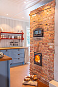 Kitchen with wood-burning stove and exposed brick wall, blue cupboards and open shelves