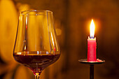 Brennende rote Kerze neben einem Glas mit Rotwein in Weinkeller
