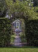 Garden path with gravel and arbour arch leading to a greenhouse with seating area