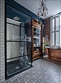 Bathroom with patterned floor tiles, freestanding copper bathtub and antique display cabinet