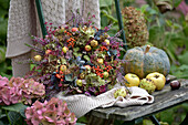 Bunter Herbstkranz aus Hortensien (Hydrangea), Samenkapseln, Heidekraut, Zieräpfeln, Kürbis und Vogelbeeren auf Holzstuhl