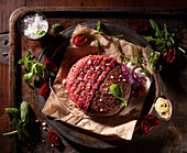 Halber roher und halber gegarter Fassona-Burger mit Meersalz, Rucola, gerösteten Tomaten, Senf und roten Zwiebelringen