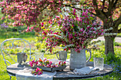 Blumenstrauß aus Zierapfelblüte (Malus) 'Paul Hauber', Brautspiere (Spiraea arguta) und Gräsern auf Gartentisch