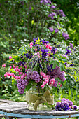 Strauss aus Flieder (Syringa), Tränendes Herz (Lamprocapnos spectabilis), Hafergras, Akelei (Aquilegia) in Vase auf Gartentisch