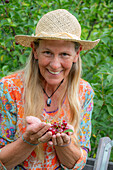 Woman harvesting cherries (Prunus Avium) and holding fruit in her hands, portrait