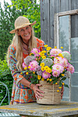 Frau mit sommerlichen Strauß mit Färber-Hundskamille, Dahlie (Dahlia), Zierlauch (Allium) auf der Terrasse