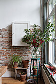 Bouquet of red berries and green branches in glass vase, plants and brick wall