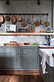 Country kitchen with green-grey cupboards, copper cookware on wall bracket and wooden floor