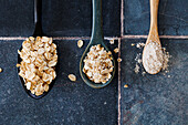 Three spoons with rolled oats and oatmeal on a stone base