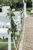 White chairs decorated with eucalyptus branches for an outdoor celebration